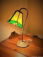 Side view of the vintage Tiffany style gooseneck table lamp turned on, showing the stained glass shade and base resting on a wooden table.