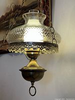 Front view of the hanging vintage electric light with hobnail pattern glass shade and brass body suspended by chain.