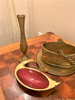 Full view of the three vintage brass items on a wooden surface: tall brass vase, swan dish, and basket on plate.