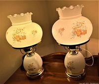Pair of illuminated vintage milk glass lamps with floral designs on both the shades and bases.