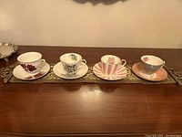 Four vintage ceramic tea cups and their matching saucers placed in a single row on a decorative tray