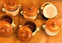 Top view of five vintage French terracotta cookware pots with lids. The pots have natural beige exteriors and brown glazed lids.