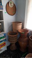 Photo showing three different wicker baskets together near a bookshelf and window. A wicker sombrero wall art piece is hung on wall above baskets.