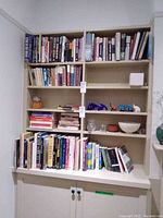 Bookshelf with multiple shelves containing assorted books of different sizes, colors, and thicknesses. Some decorative items on shelves not included in sale.