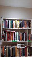 Three shelves filled with hardcover and some paperback books, showing spine titles and colors