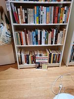 Three shelves filled with various books by multiple authors arranged on white shelving unit.