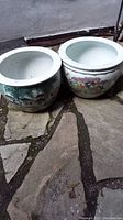 Photo of two white ceramic planters with Asian style painted designs placed on stone ground.