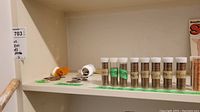 Photo shows shelf with multiple rolled tubes of coins marked with labels indicating contents such as '39', '29', '78', '61', etc. Also visible loose coins scattered on the shelf including some large silver-colored coins and copper pennies.