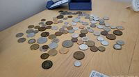 Photo showing a large assortment of coins laid out on a table surface, differing in size and metallic color.