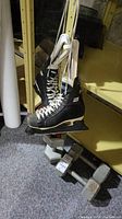 Pair of black CCM Pro ice hockey skates hanging, size approximately 9, paired with three 20 lb hexagonal dumbbells arranged below them.
