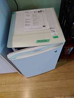 Front and top view of white Danby bar fridge with user manual on top