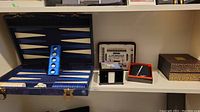 Shelf view showing backgammon set open with playing pieces and dice, Autobridge game box, Rawlings wallet and note paper holder set