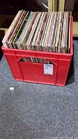 Red crate filled with many LP vinyl records seen from one side showing the spines of the albums.