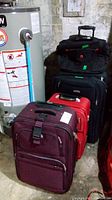 All three luggage bags stacked near a water heater in a basement, showing the variety of sizes and colors.