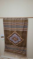Full view of handmade Mexican rug with geometric pattern and fringe at wall mount.