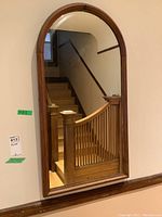 Front view of arched mirror showing wood frame and reflection of staircase.
