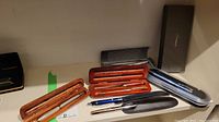 Photo showing multiple pen sets and letter opener, with wooden and metal cases.
