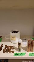 White plastic container labeled 'PENNIES' filled with old pennies, loose US pennies spread out on shelf, and a small vial with label 'US Pennies 1950-1964'.