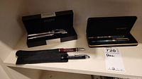 Photo of Balmain pen and pencil silver-tone set in original black box, and two loose pens in black fabric sleeves marked McMaster and University of Toronto.