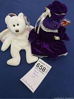 Two Beanie Babies plush toys: white angel bear and purple velvet bear in dress, with lot tag included.