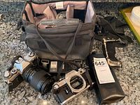 Photo showing Canon AT-1 camera body, two lenses, camera bag and Canon lens case with strap.