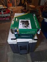 Photo showing Wild River 12-piece campfire essential set box on top of a Coleman cooler, with the cooler and folding chair visible in the background.