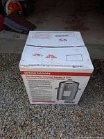 Boxed Brinkmann charcoal smoker and grill unit shown on gravel, box marked fragile and directions.