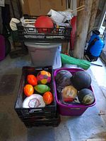 Photo showing crates with assorted sports balls, a red ball, and other items stored in a plastic crate and tub.