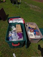 Two large plastic totes filled with assorted Christmas decorations placed outdoors on grass.