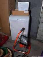 White Danby Premiere dehumidifier with grille front, orange and black Power Glow job light on floor in front, along with boxed driveway alert system and packaging on top of dehumidifier.