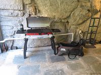 Thermos Grill 2 Go portable gas grill set up with carrying bag beside it on floor in stone-floored area.