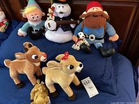 Full set of seven vintage-style holiday plush toys including Rudolph, Clarice, Yukon Cornelius, snowman with banjo, bearded figure, spotted dog, and Bumble the Snow Monster.