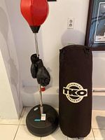 Freestanding orange speed punching bag with chrome stand and black weighted base, black boxing gloves hanging from stand.