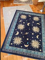 Two rugs visible: celestial themed 5x7 navy blue rug with sun, moon, stars, planets, and a light beige traditional patterned 5x8 rug beneath it on wooden floor.