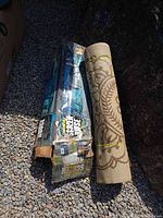 Boxed convertible screen house and rolled indoor/outdoor rug on gravel ground.