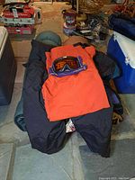 Sleeping bags, orange Guess nylon pants, and Cebe snow goggles arranged on floor