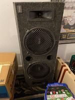 Front view of the black carpet-covered speaker cabinet with three drivers (tweeter, midwoofer with grille, woofer) and two port holes on the front.