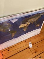 Large framed world map print titled 'The Earth From Space' leaning against wall on wooden floor