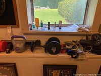 Photo of various weights including kettlebell, dumbbells, barbell with plates, ankle weights placed on a white surface in front of a window