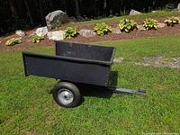 Side view of steel utility trailer with black steel bed and inflatable tire standing on grass.