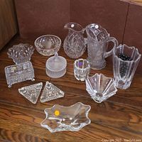Full lot view showing eleven crystal pieces including pitchers, vases, bowls, and dishes arranged on wood surface.