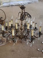 Front view of a vintage multi-arm chandelier with several candle-style bulb holders, some bulbs missing, and clear crystal drop decorations.