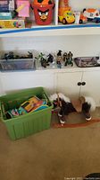 Shelf and floor view showing a variety of children's toys including toy bins, action figures on shelf, and a plush rocking horse on wooden rockers on the floor.