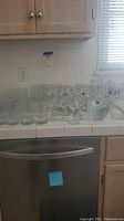 Wide view of assorted clear glassware including tumblers, stemmed glasses, and pitchers on a kitchen counter.