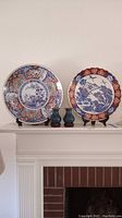 Two large decorative Japanese plates and two small blue decorative vases displayed on mantel.