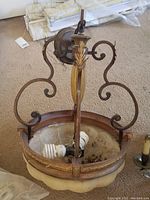 View of metal and glass chandelier showing metal scroll arms, gold leaf decorative elements, and glass bowl with light bulbs.