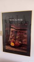 Framed 'Mexicali Rose' wall art hanging on a wall, showing detailed western-style cowboy boots with yellow rose and textile background.
