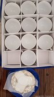 Box with 12 white porcelain saucers with floral decoration, organized in compartments.