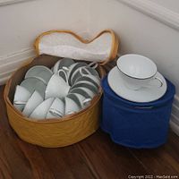 Multiple white porcelain tea cups and saucers with silver trim arranged in a yellow quilted round case and one pair displayed on a blue round case.