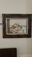Framed original seascape painting hung on wall, showing boat, pier and buildings near water.